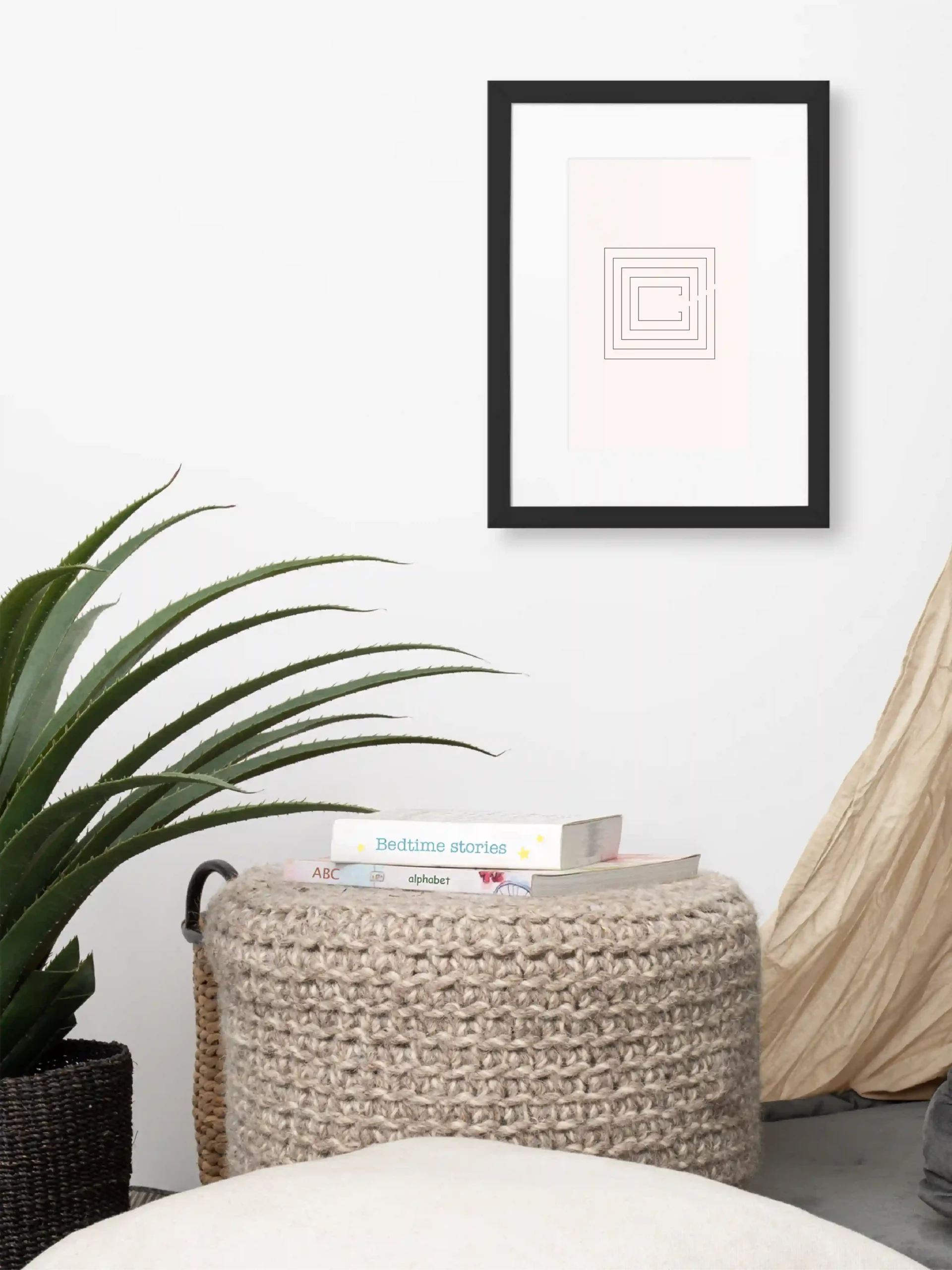 Second Look framed artwork above woven ottoman beside a large green plant